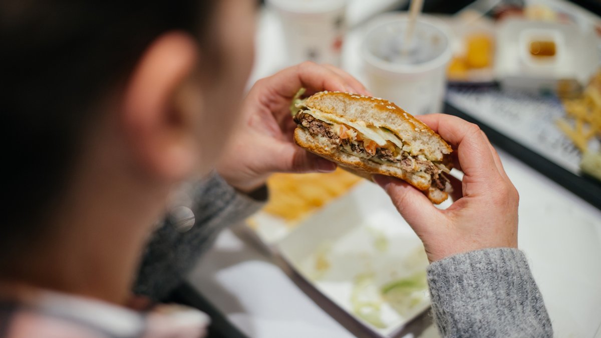 Eine Frau isst einen Hamburger bei einer Fast-Food-Kette.