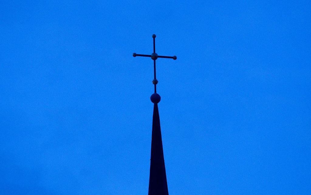 Ein Kirchenkreuz ragt in den blauen Himmel. 