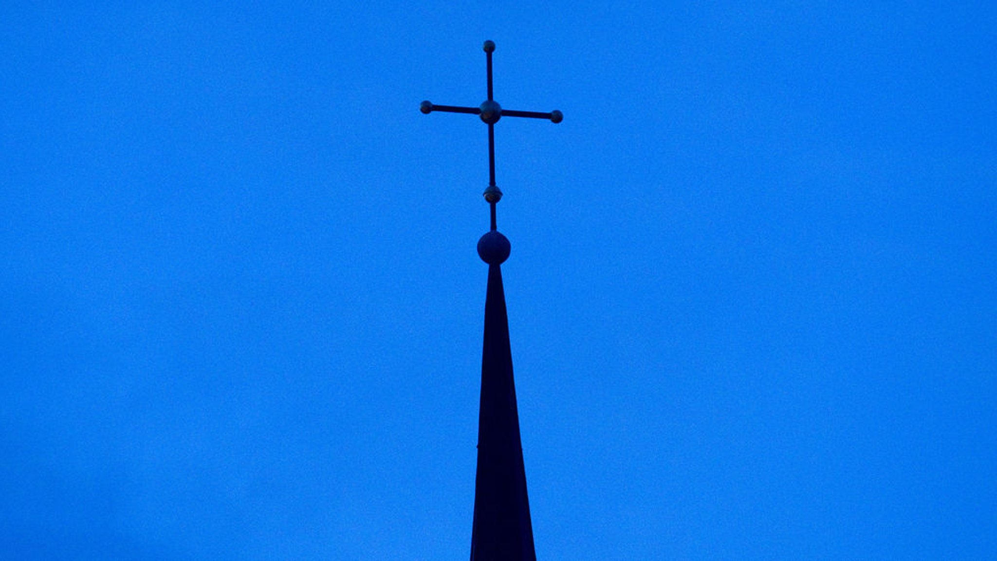 Ein Kirchenkreuz ragt in den blauen Himmel. 