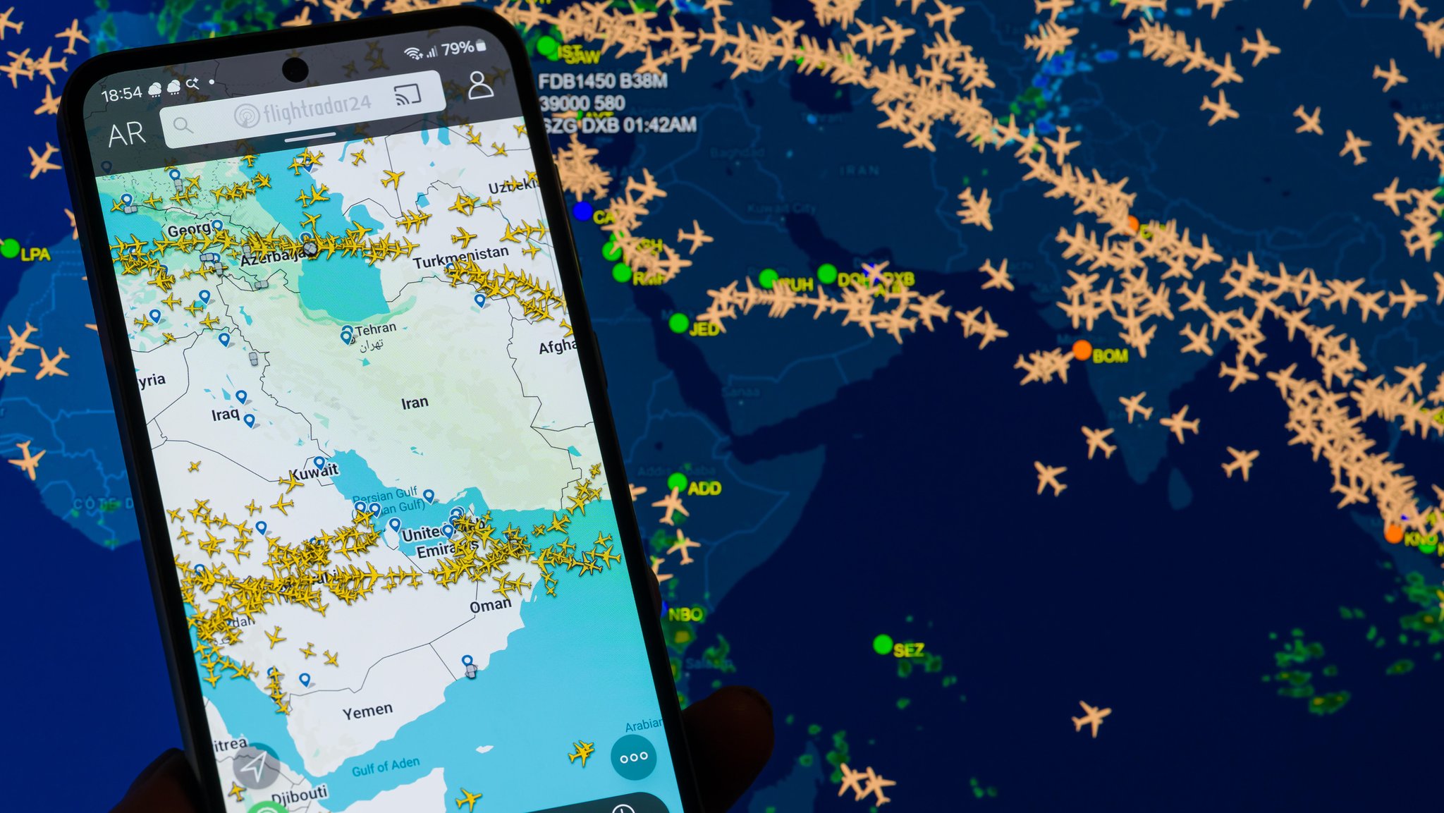 Eine Karte auf Laptop und Smartphone zeigt den Flugverkehr über dem Nahen Osten, während Airlines wegen des Konflikts mit Iran Flüge umleiten oder streichen.