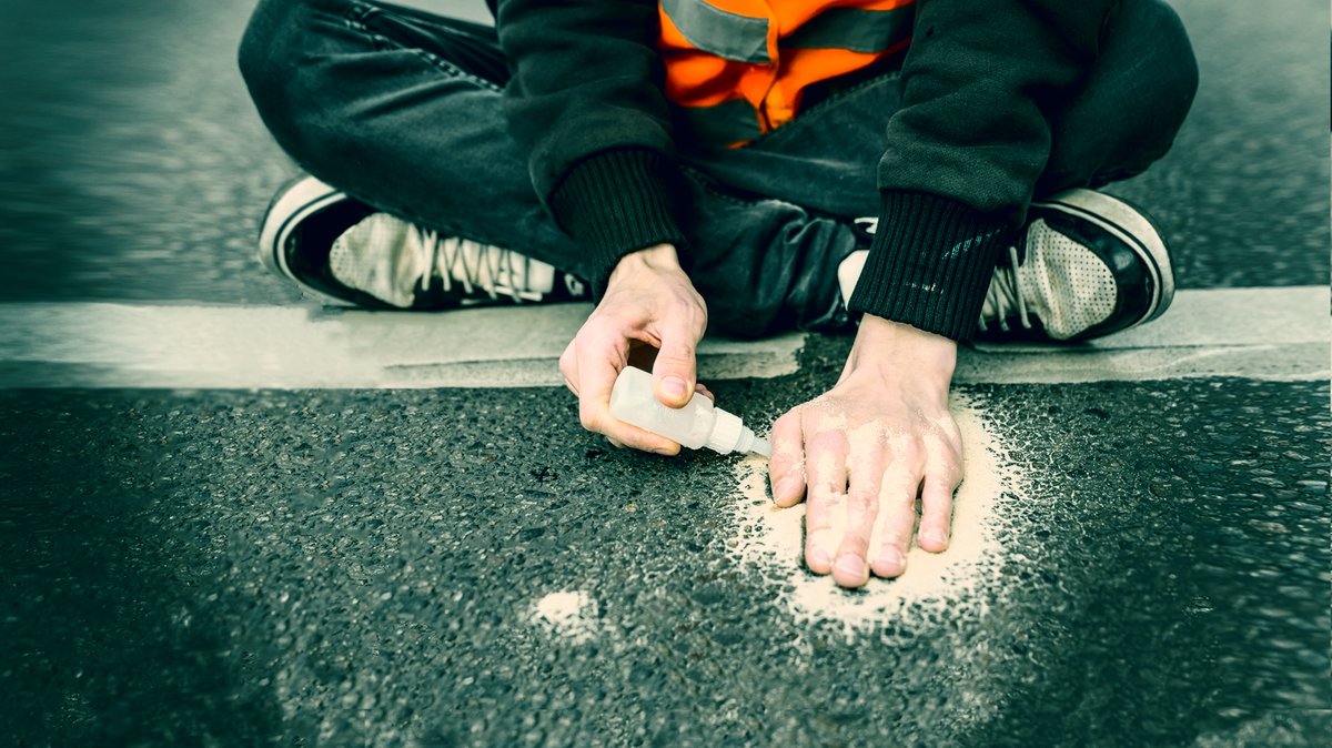Ein Aktivist der Letzten Generation klebt sich die Hand mit Sekundenkleber auf der Straße fest.