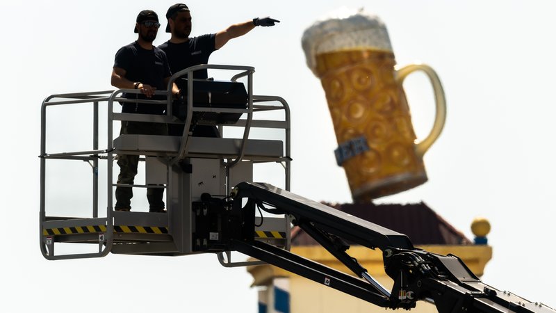 Aufbauarbeiten fürs Oktoberfest 2022: Zwei Arbeiter auf einem Kran, dahinter eine überdimensional große Maß Bier.