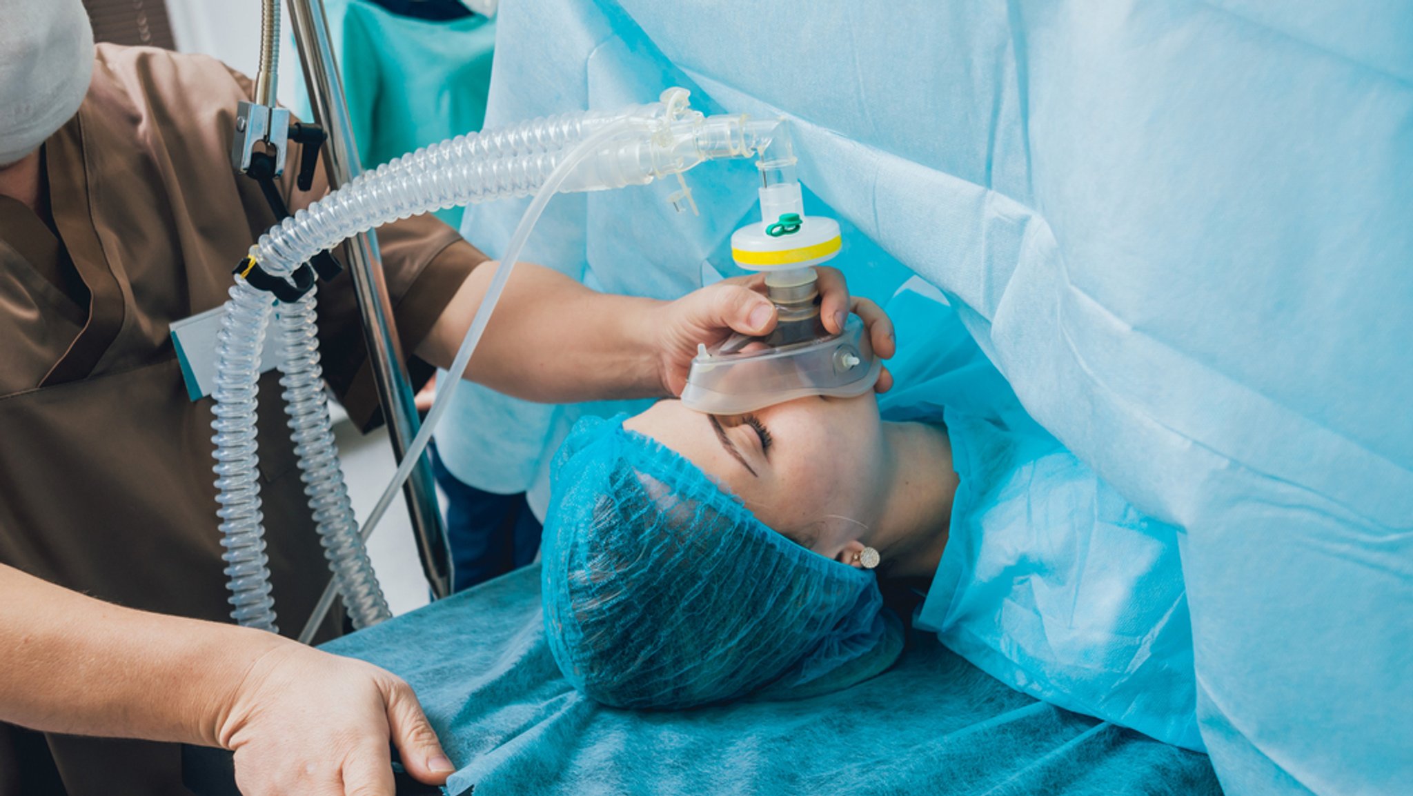  Patientin liegt auf einem Operationstisch und erhält über eine Beatmungsmaske Narkose.