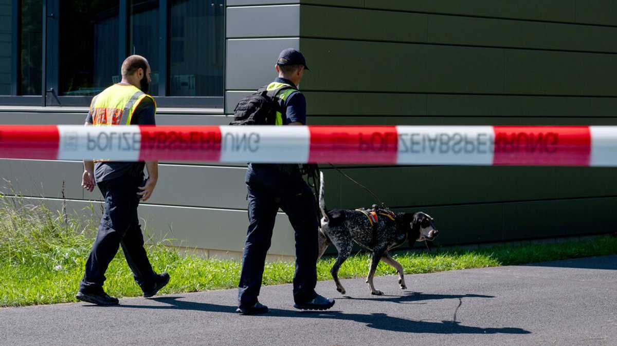 09.09.2023, Bayern, Lohr Am Main: Mit einem Spürhund durchsuchen Polizeibeamte das Gebiet am Schulzentrum in Lohr am Main. Tags zuvor war hier ein toter Jugendlicher gefunden worden. Foto: Pia Bayer/dpa +++ dpa-Bildfunk +++