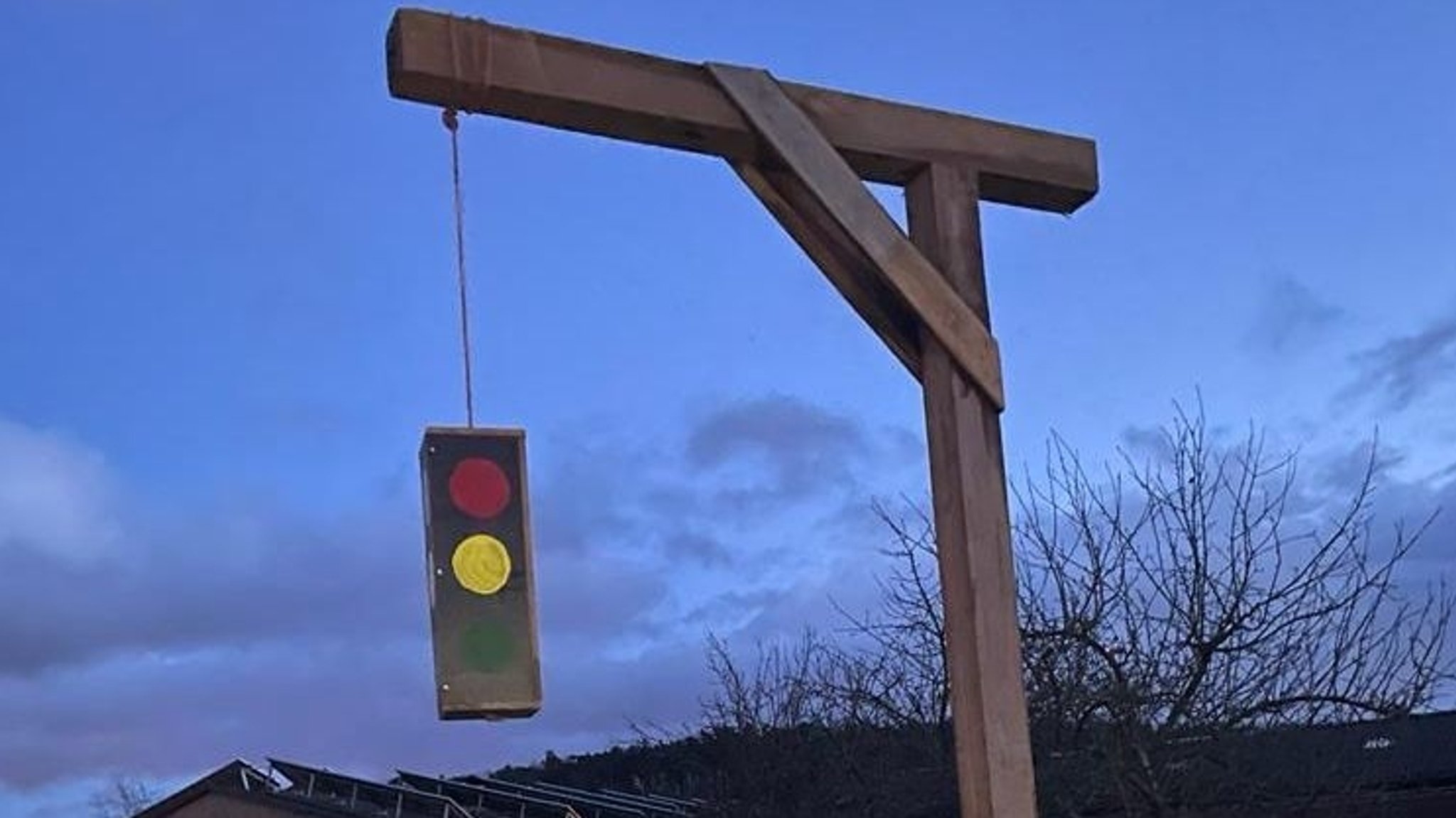 Ein hölzerner Galgen vor dem Abendhimmel, an dem eine Ampel hängt.