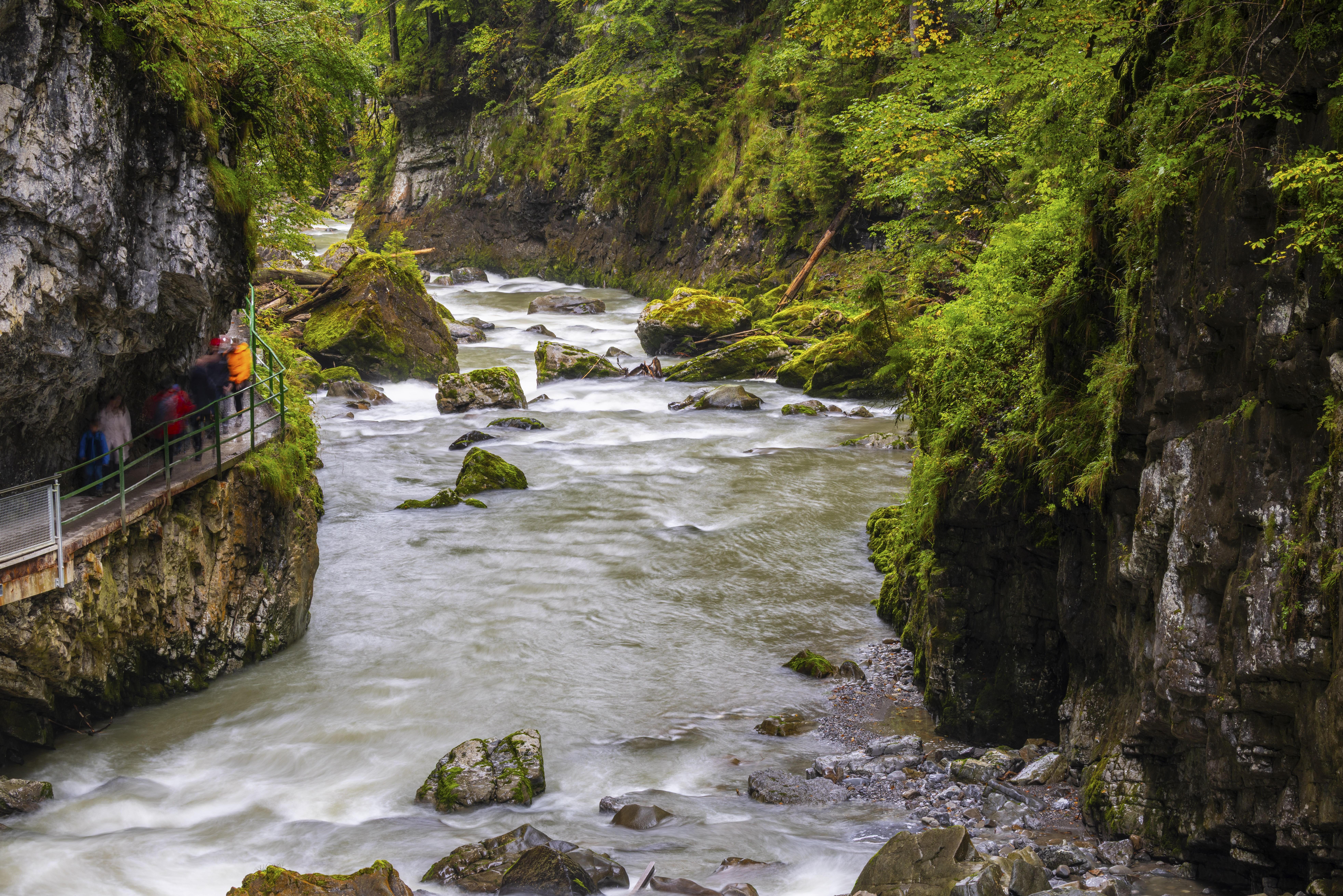 Ein Fluss fließt durch eine sich verengende Klamm. Besucher gehen neben dem Fluss auf einem Steg entlang.