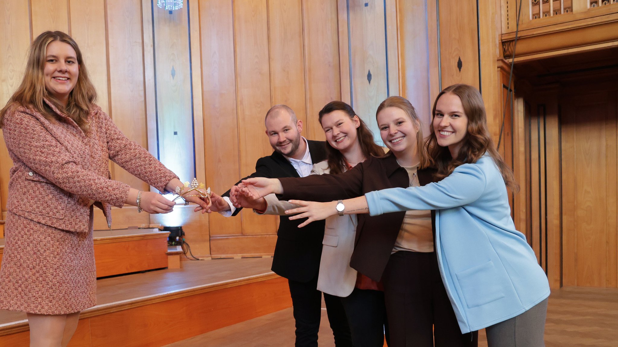Die Weinkönigin Antonia Kraiß hält ihre Krone vor sich. Die Weinprinzessinen und der Weinprinz greifen danach. | Bild: Rudi Merkl / Fränkischer Weinbauverband e.V. Die Weinkönigin Antonia Kraiß hält ihre Krone vor sich. Die Weinprinzessinen und der Weinprinz greifen danach.