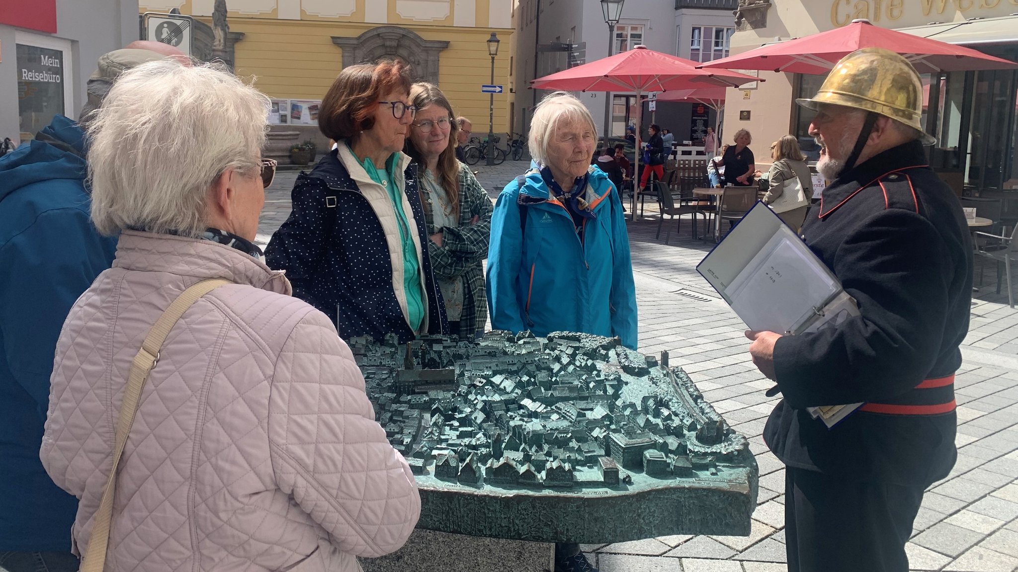 Mit goldenem Helm und schwarzem Hemd gekleidet zeigt der frühere Stadtbrandmeister Anton Heider Teilnehmern seiner Stadtführung das Kaufbeurer Stadtmodell.