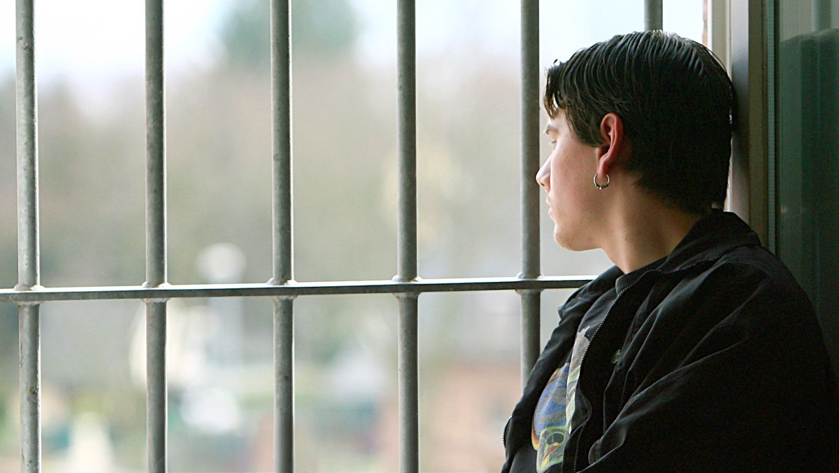 Symbolbild: Ein jugendlicher Insasse einer Justizvollzugsanstalt sitzt auf einer Fensterbank und schaut aus dem Fenster