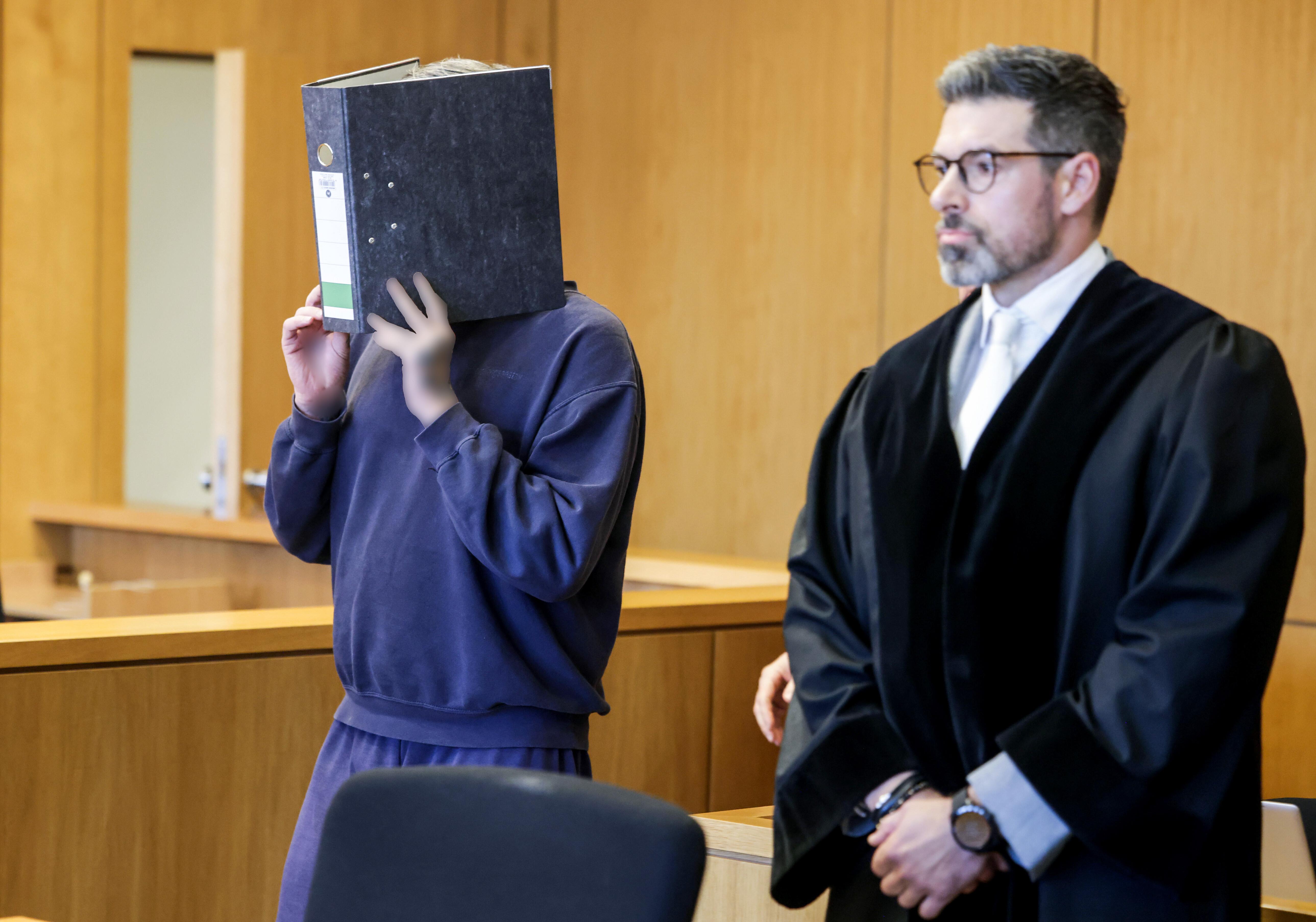 05.11.2025: Der Angeklagte Krankenpfleger hält sich einen Aktenordner vor das Gesicht. Die Hände wurden aus rechtlichen Gründen gepixelt. 