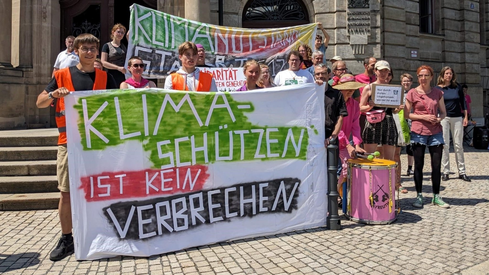 Mehrere Menschen halten Transparente hoch. Auf einem steht: Klimaschützen ist kein Verbrechen.