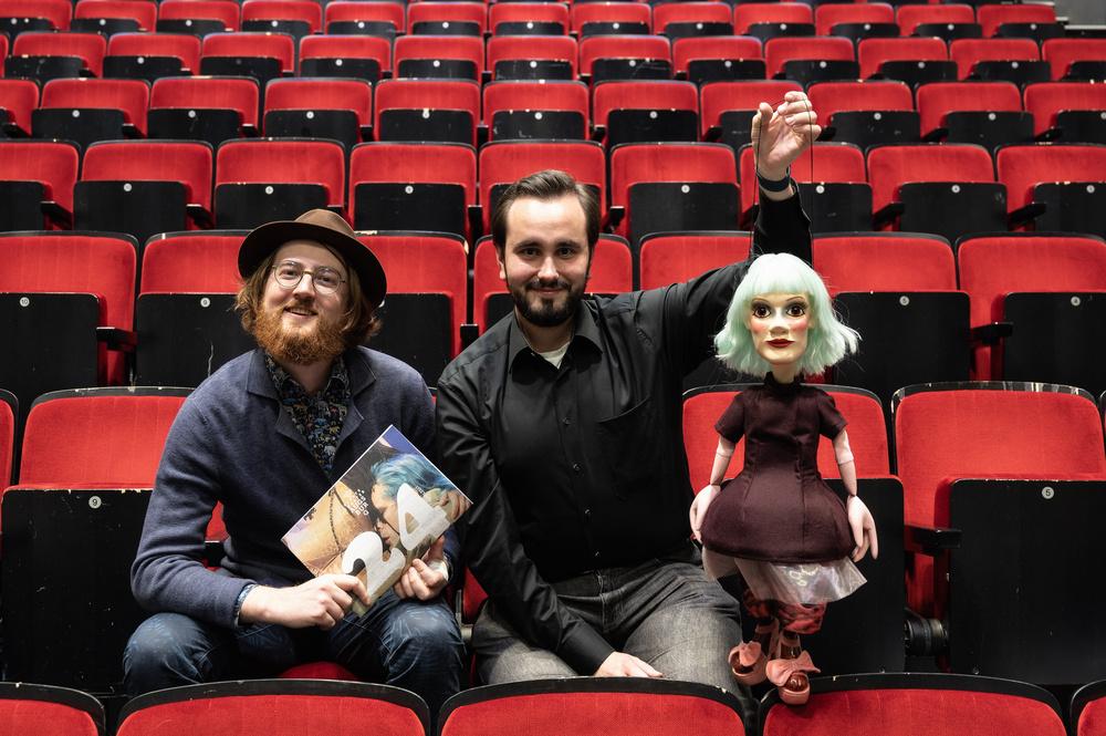 Lukas Joshua Baueregger (Produktionsleitung) und Benjamin Seuffert (Technische Realisation) mit einer Puppenkisten-Marionette und dem Programmheft zur Spielzeit 2024/25 des Staatstheaters Augsburg