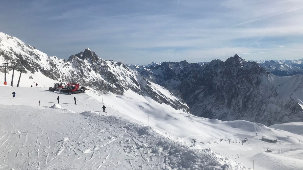 Ein Skigebiet mit vereinzelten Snowboardern und Skifahrern auf der Piste. Im Hintergrund ist ein Sessellift und eine Schneeraupe zu sehen. 