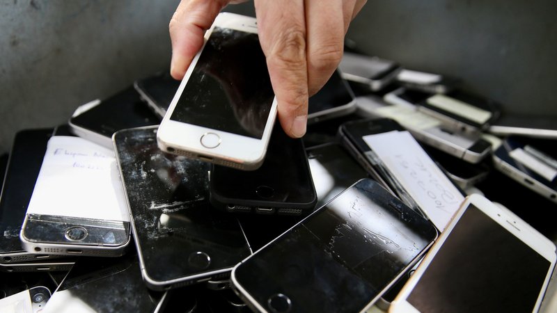 Eine Hand lässt ein iPhone auf einen Berg anderer ausrangierter Smartphones fallen | Bild: picture alliance / Cem Ali Kus Eine Hand lässt ein iPhone auf einen Berg anderer ausrangierter Smartphones fallen