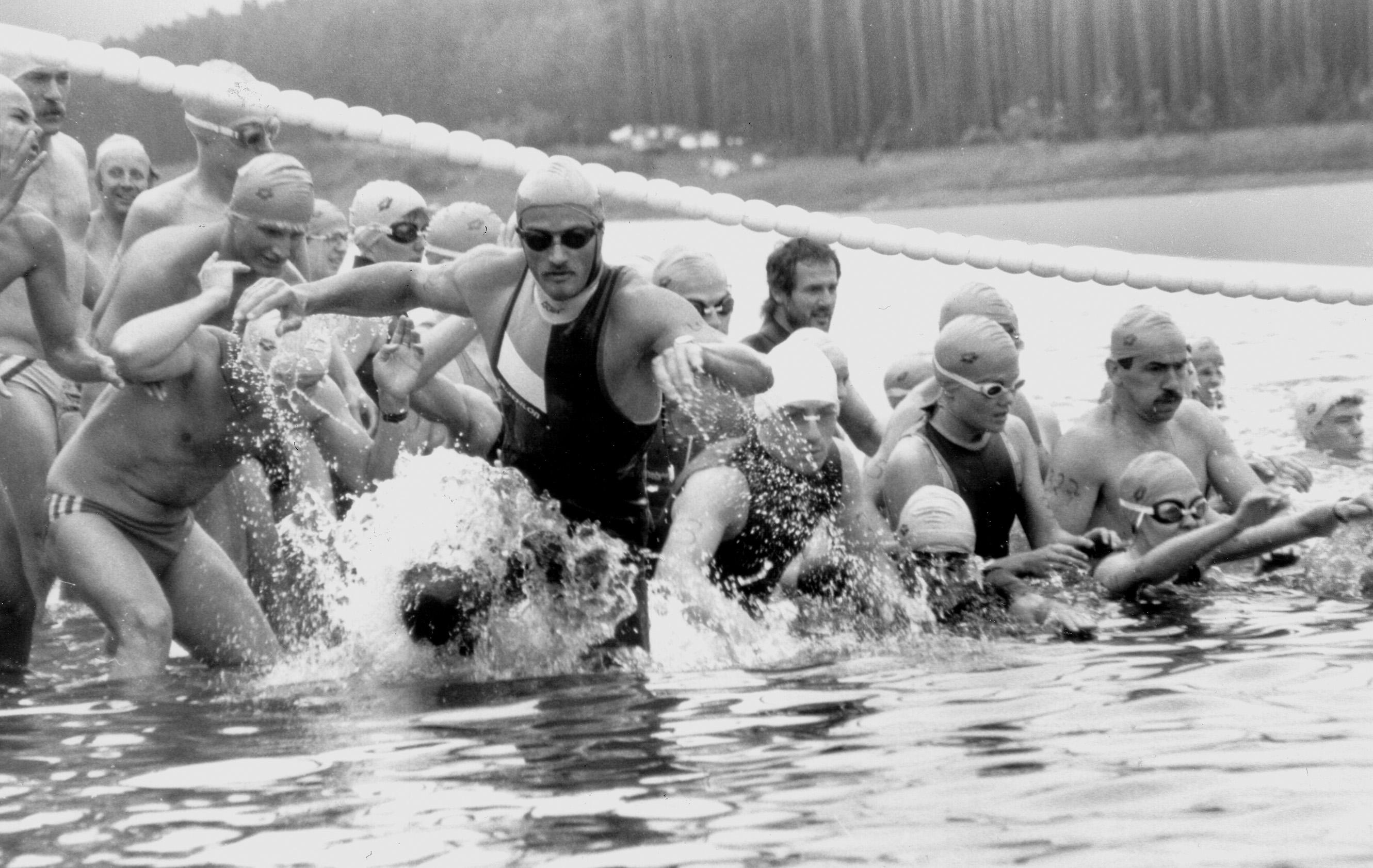 Bild in Schwarzweiß: Schwimmer im Wasser machen sich für den Triathlon 1984 bereit.