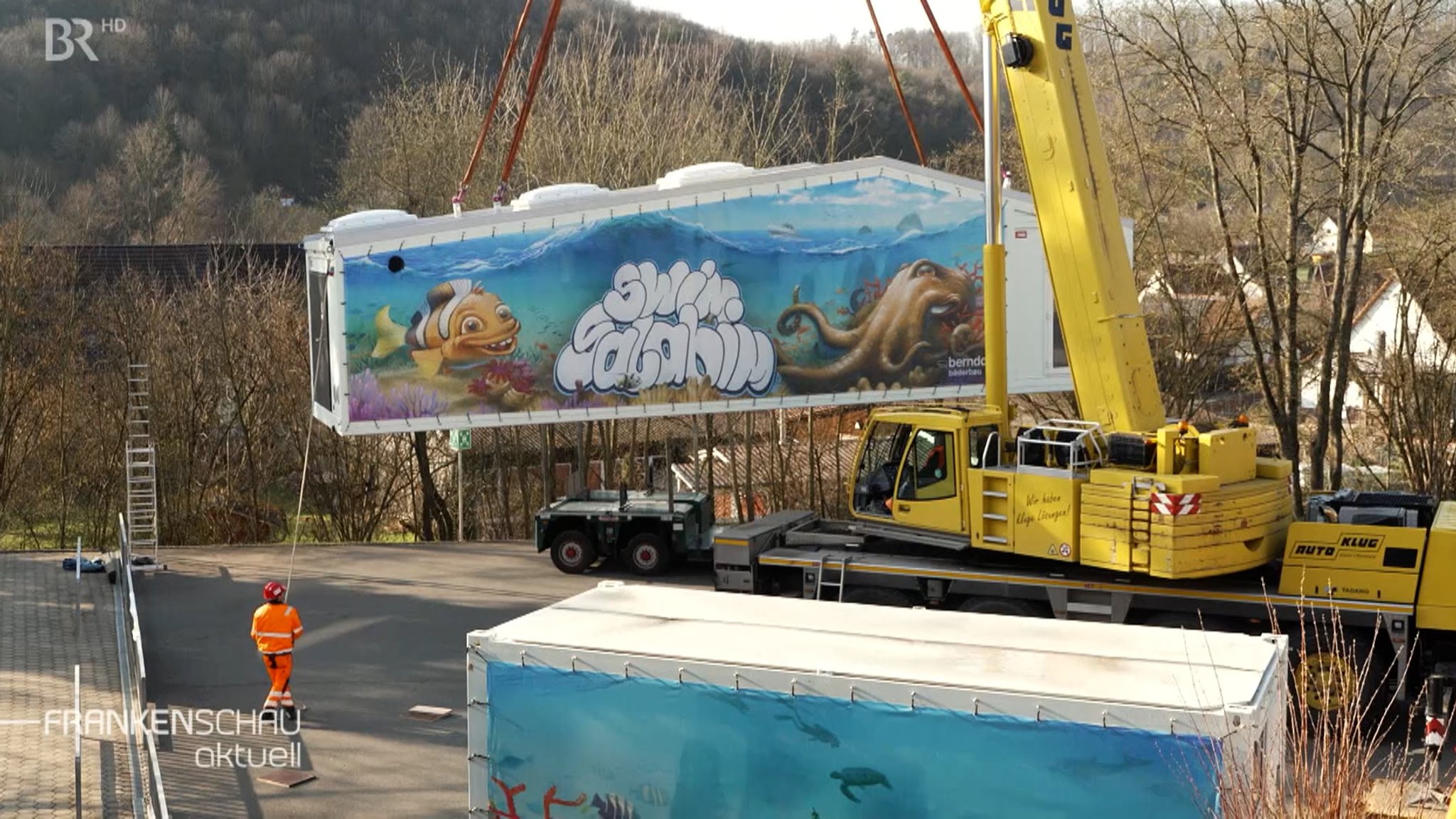 Ein Schwimmbad-Container wird mithilfe eines Krahnes aufgestellt.