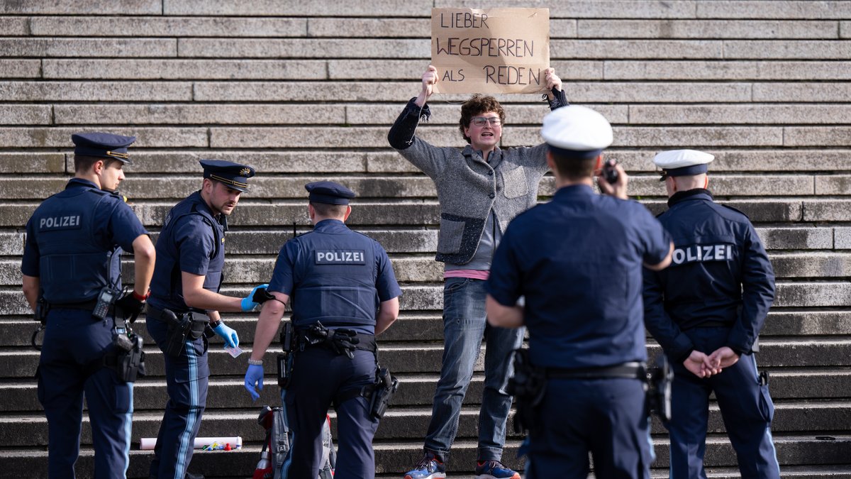 Klimaaktivisten der Protestgruppe "Letzte Generation" demonstrieren vor der bayerischen Staatskanzlei und halten ein Schild mit der (ironischen) Aufschrift "Lieber wegsperren als reden" in den Händen.
