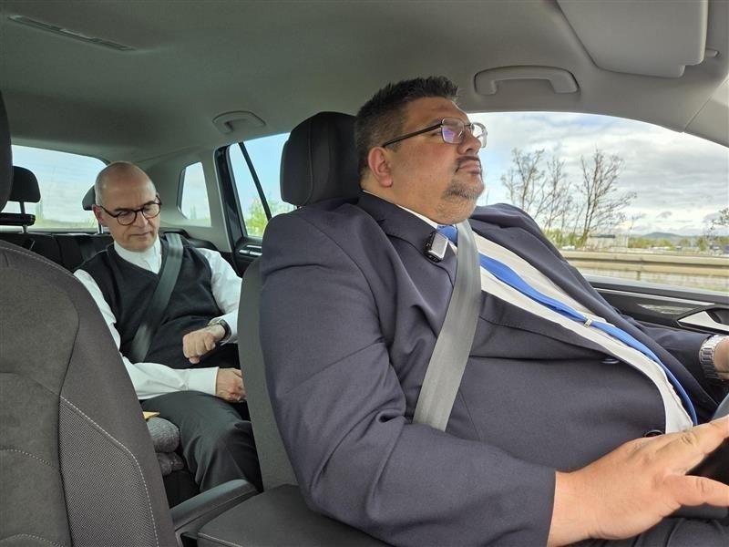 Dominik Zeißner sitzt am Steuer eines Autos. Auf dem Rücksitz sitzt der Würzburger Bischof Franz Jung.