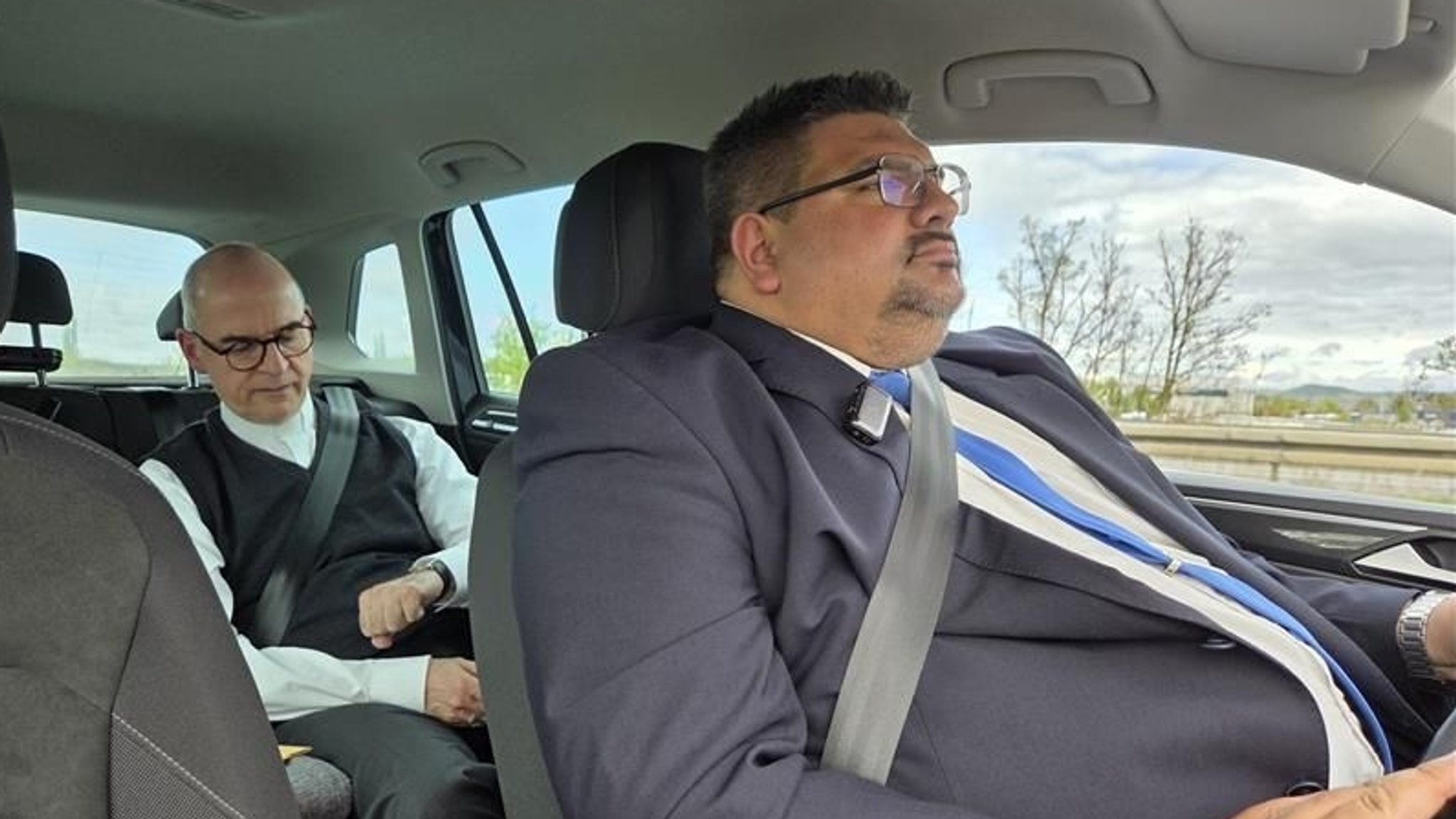 Dominik Zeißner sitzt am Steuer eines Autos. Auf dem Rücksitz sitzt der Würzburger Bischof Franz Jung.