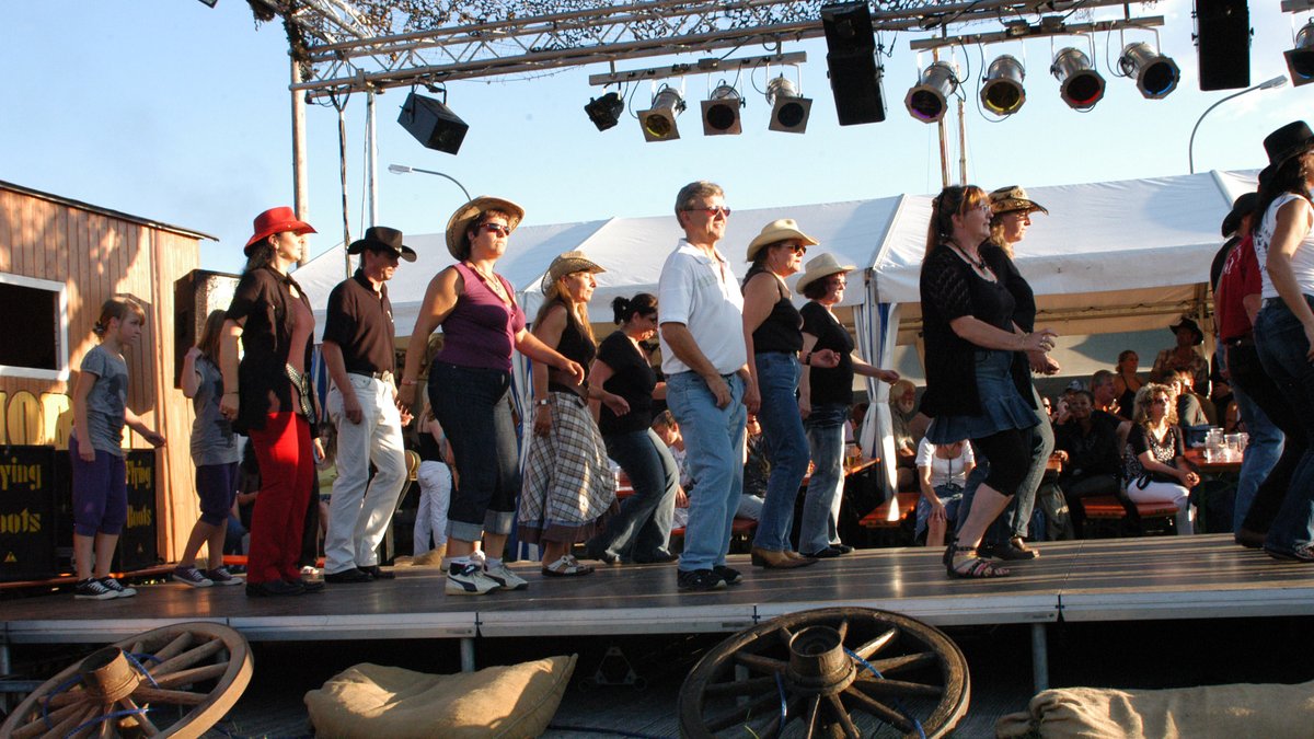 Frauen und Männer, teils mit Cowboy-Hüten, tanzen den sogenannten Line-Dance, ein typisch amerikanischer Formationstanz