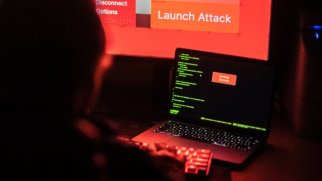 Ein aufgeklappter Laptop, dahinter ein rot leuchtender Bildschirm mit der Aufschrift "Launch Attack". (Symbolbild)