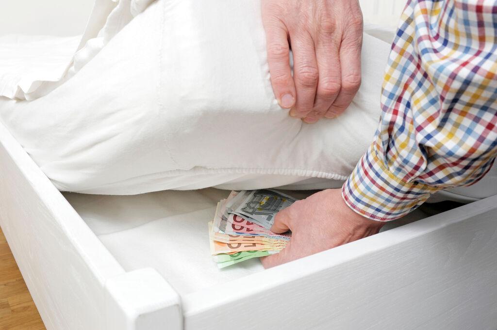 Ein Mann versteckt Bargeld unter einer Matratze.