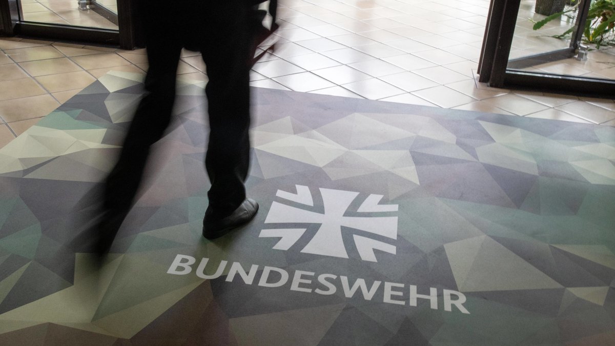 Ein Fußbodenteppich in Tarnfarben, darauf der Schriftzug "Bundeswehr". Eine Person in Bewegungsunschärfe läuft darüber.