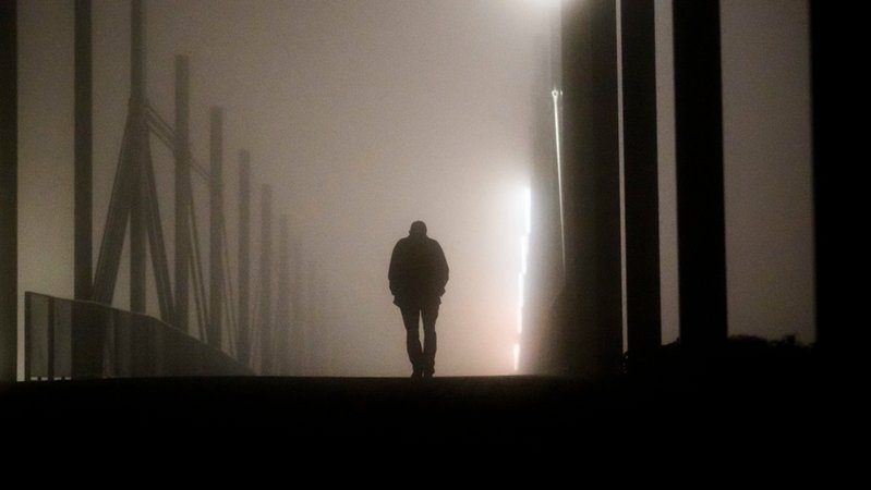 Ein Mann geht am frühen Morgen bei Nebel über eine Brücke.