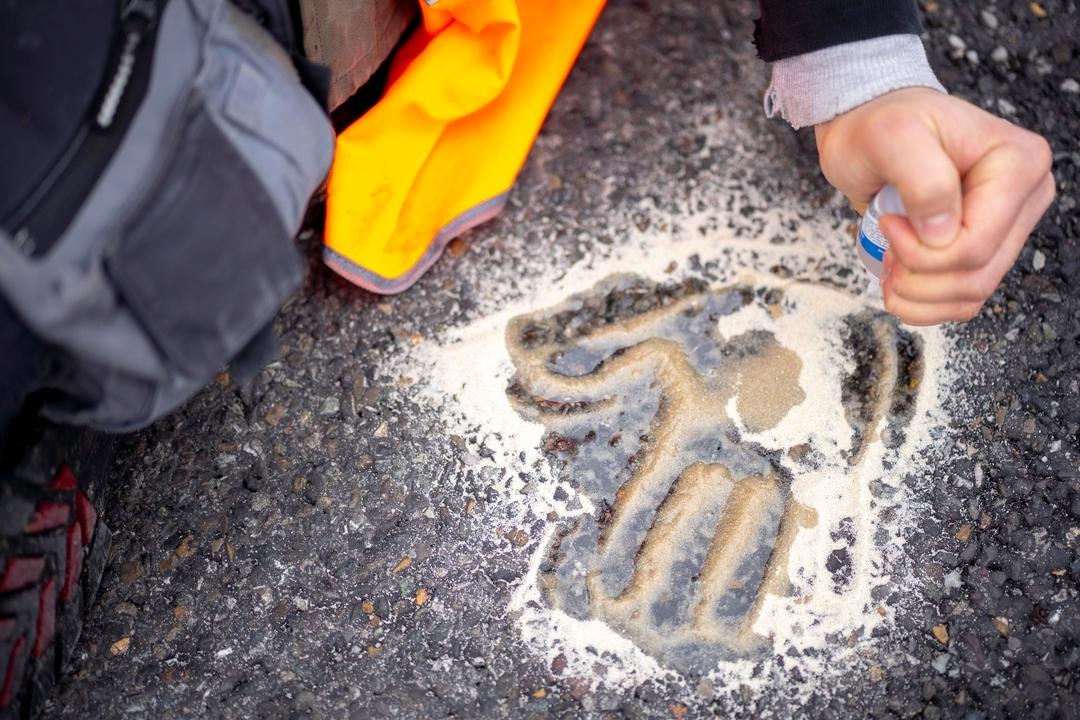 Auf dem Asphalt einer Straße ist der Handabruck eines "Klimaklebers" zu sehen
