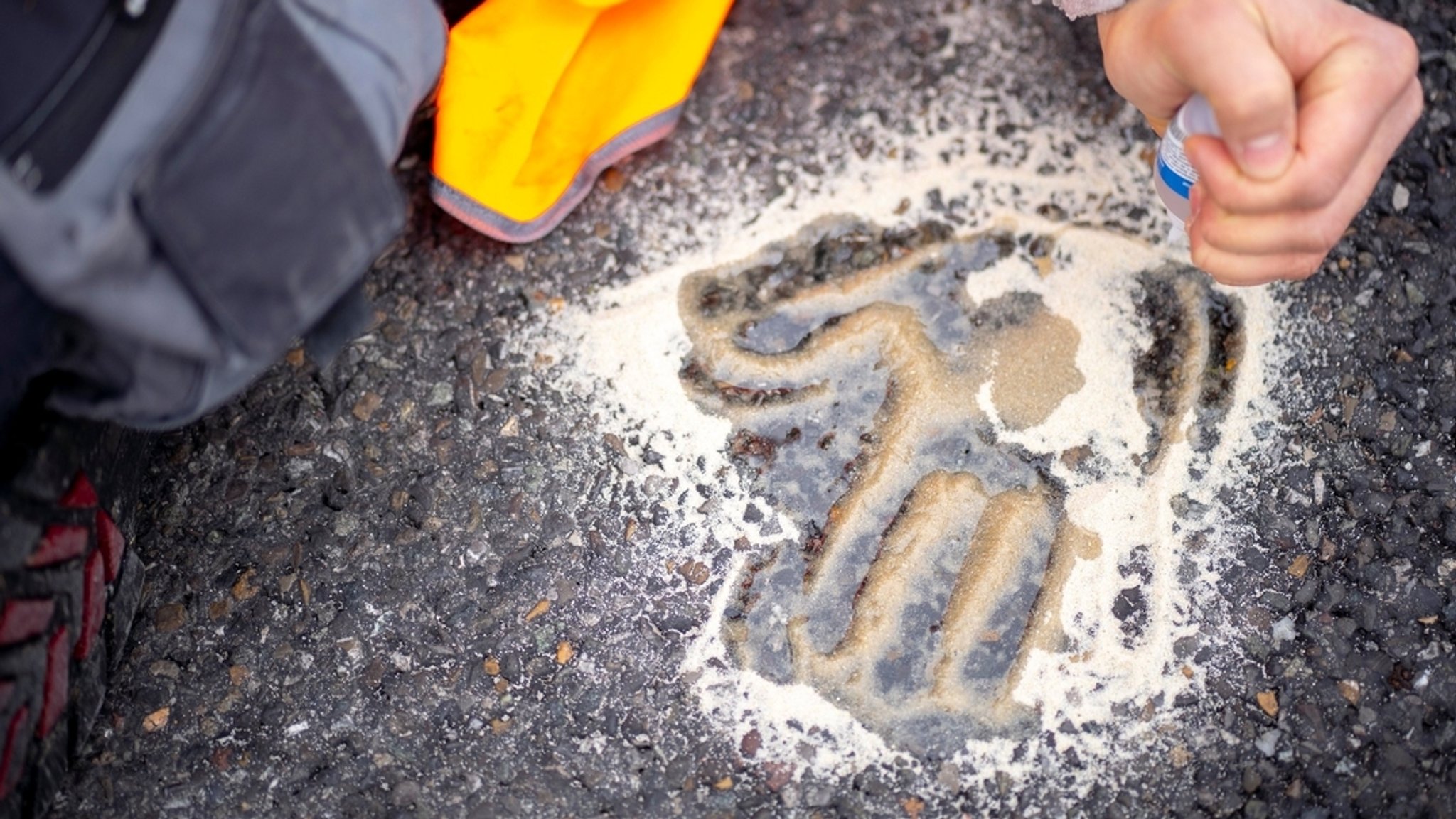 Auf dem Asphalt einer Straße ist der Handabruck eines "Klimaklebers" zu sehen