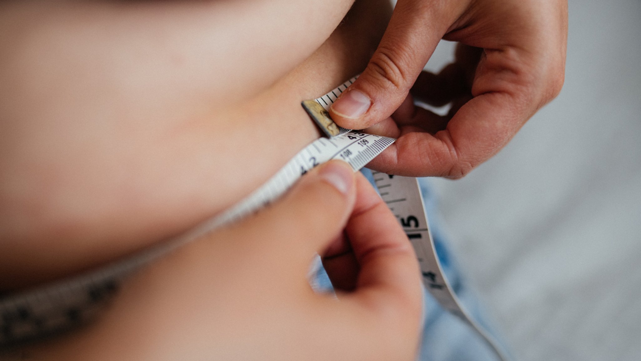 Eine Frau misst ihren Bauch mit einem Maßband.