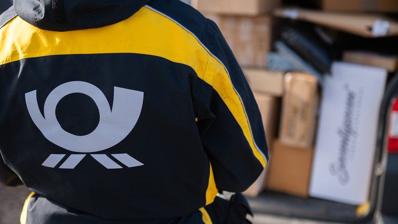 Eine Postbotin trägt eine Jacke mit dem Logo der Deutschen Post und hält dabei ein Paket vor einem Zustellfahrzeug in der Hand. | Bild: picture alliance/dpa | Silas Stein Eine Postbotin trägt eine Jacke mit dem Logo der Deutschen Post und hält dabei ein Paket vor einem Zustellfahrzeug in der Hand.
