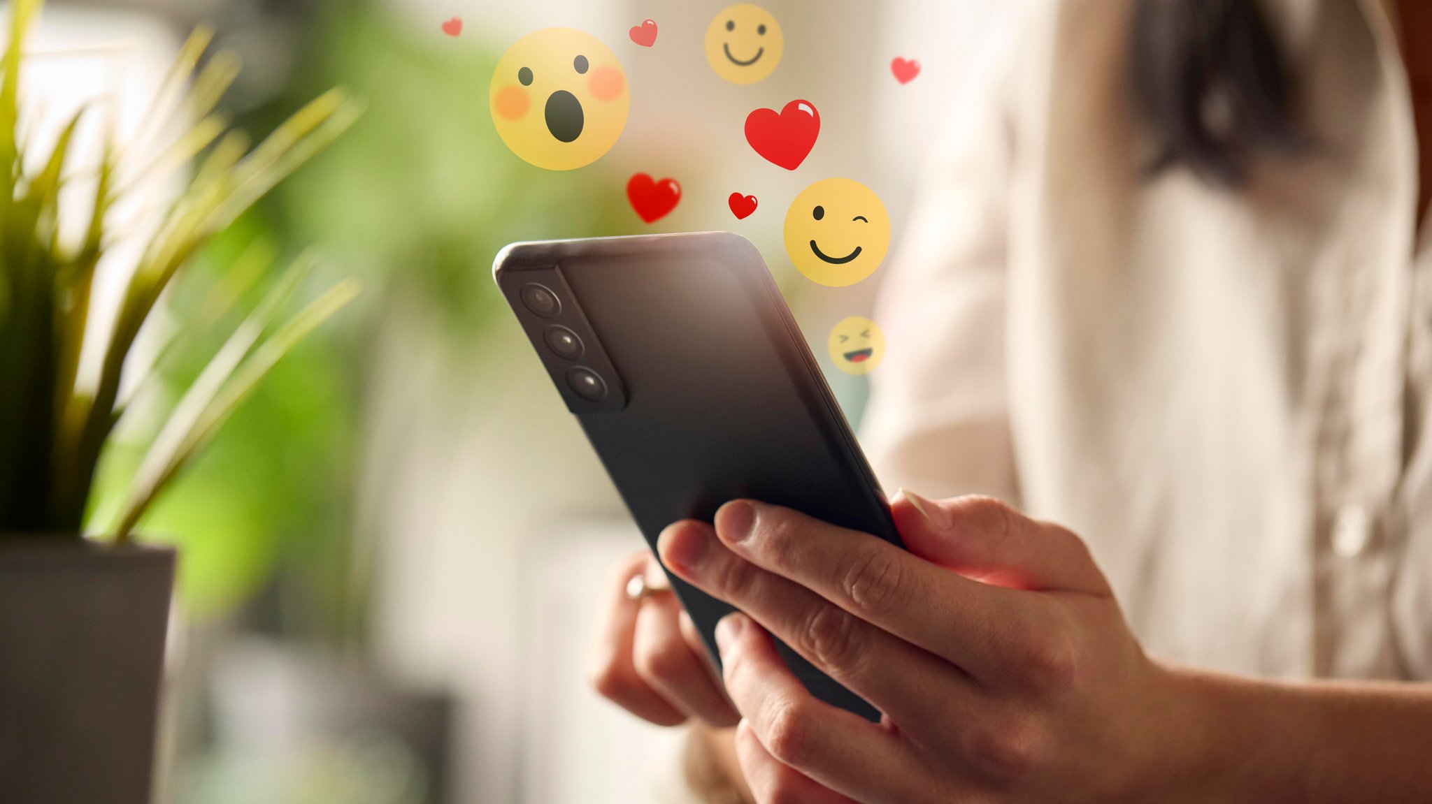Eine Frau hält ein Handy in der Hand aus dessen Display Emojis in die Luft fliegen.