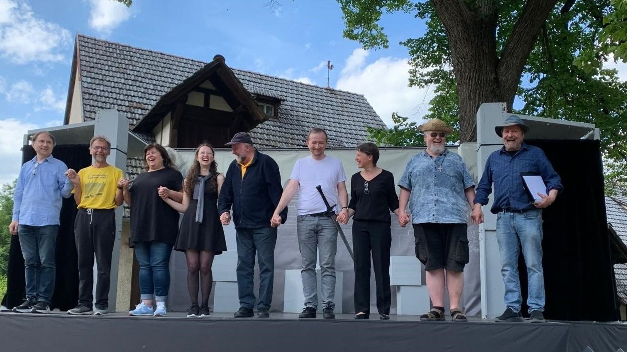 Schauspieler stehen auf einer Bühne, die vor einem Haus steht. 