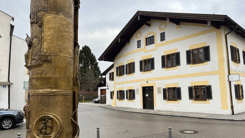 Auf dem Bild sind das Geburtshaus des emeritierten Papstes und eine goldene Steele zu sehen.
