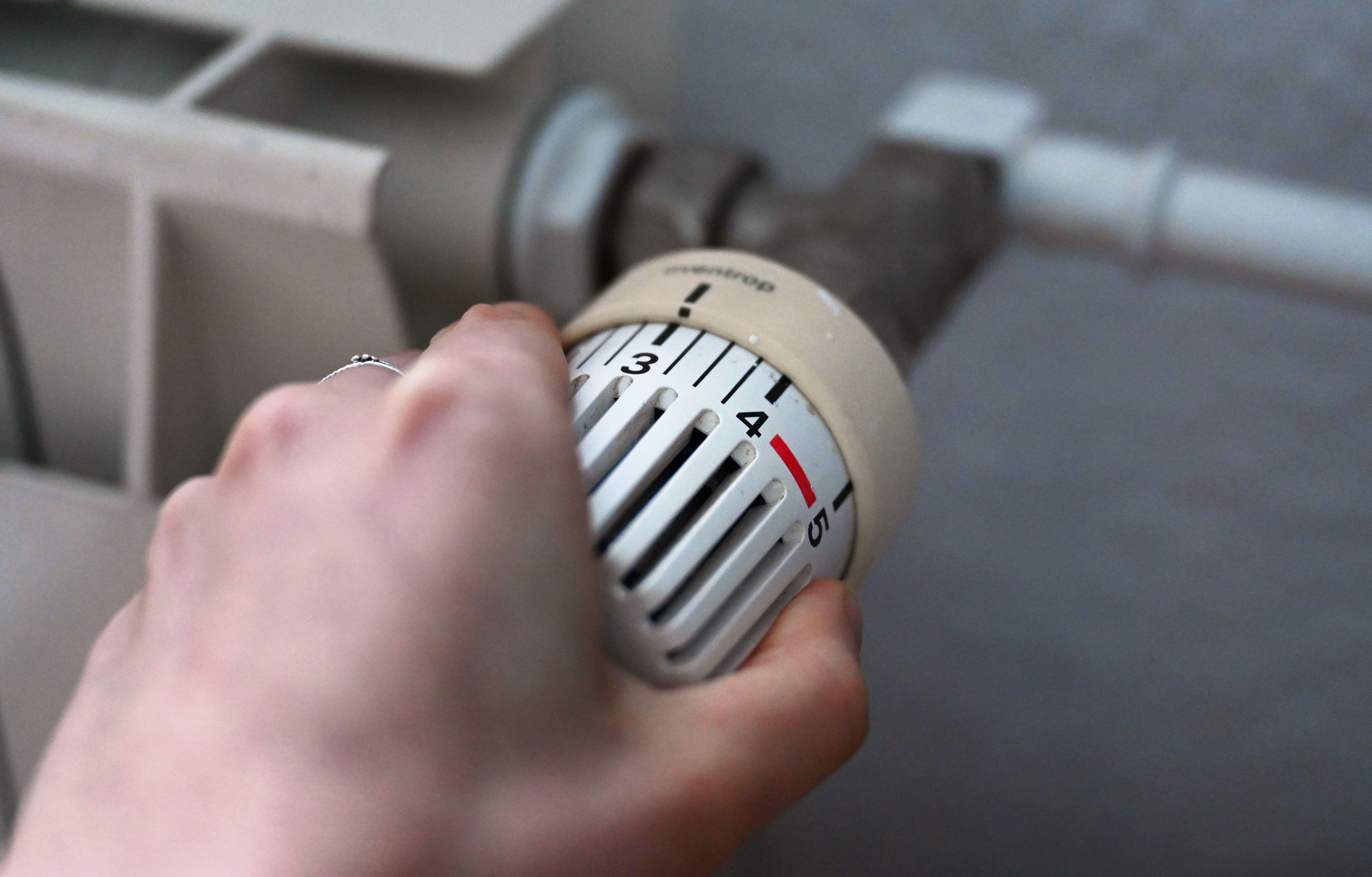 (Symbolbild) Eine Frau dreht an einem Thermostatregler einer Heizung in einer Wohnung. 