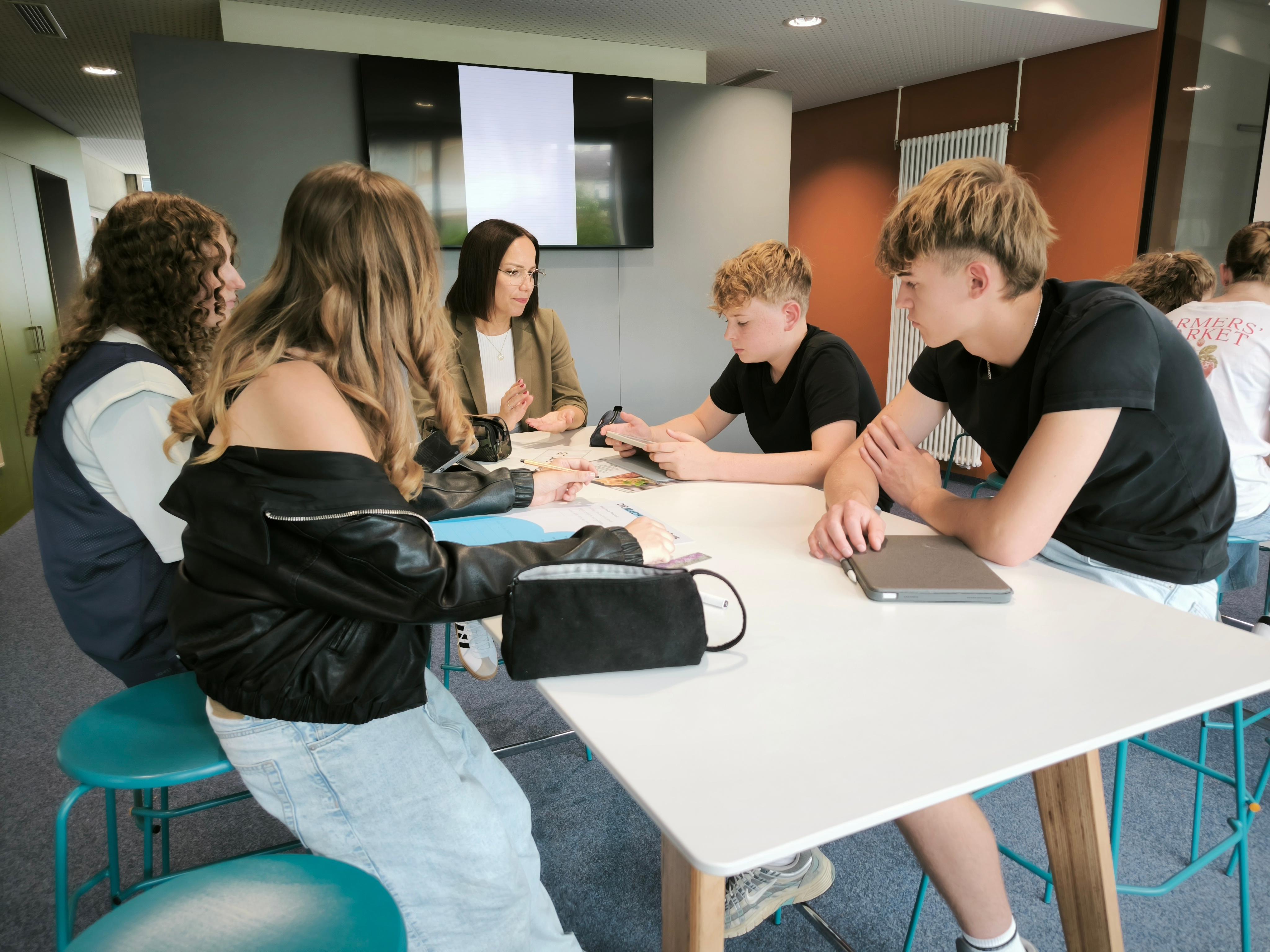 Schüler sitzen an einem Tisch mit einer Lehrerin