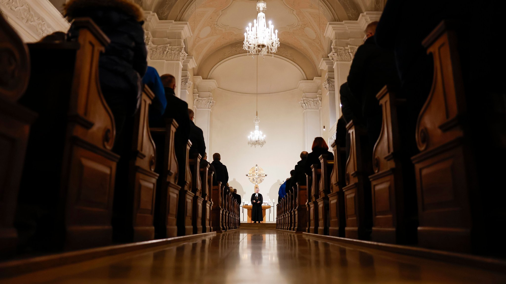 Symbolbild: Ein Pfarrer steht alleine vor den Kirchenbänken. 