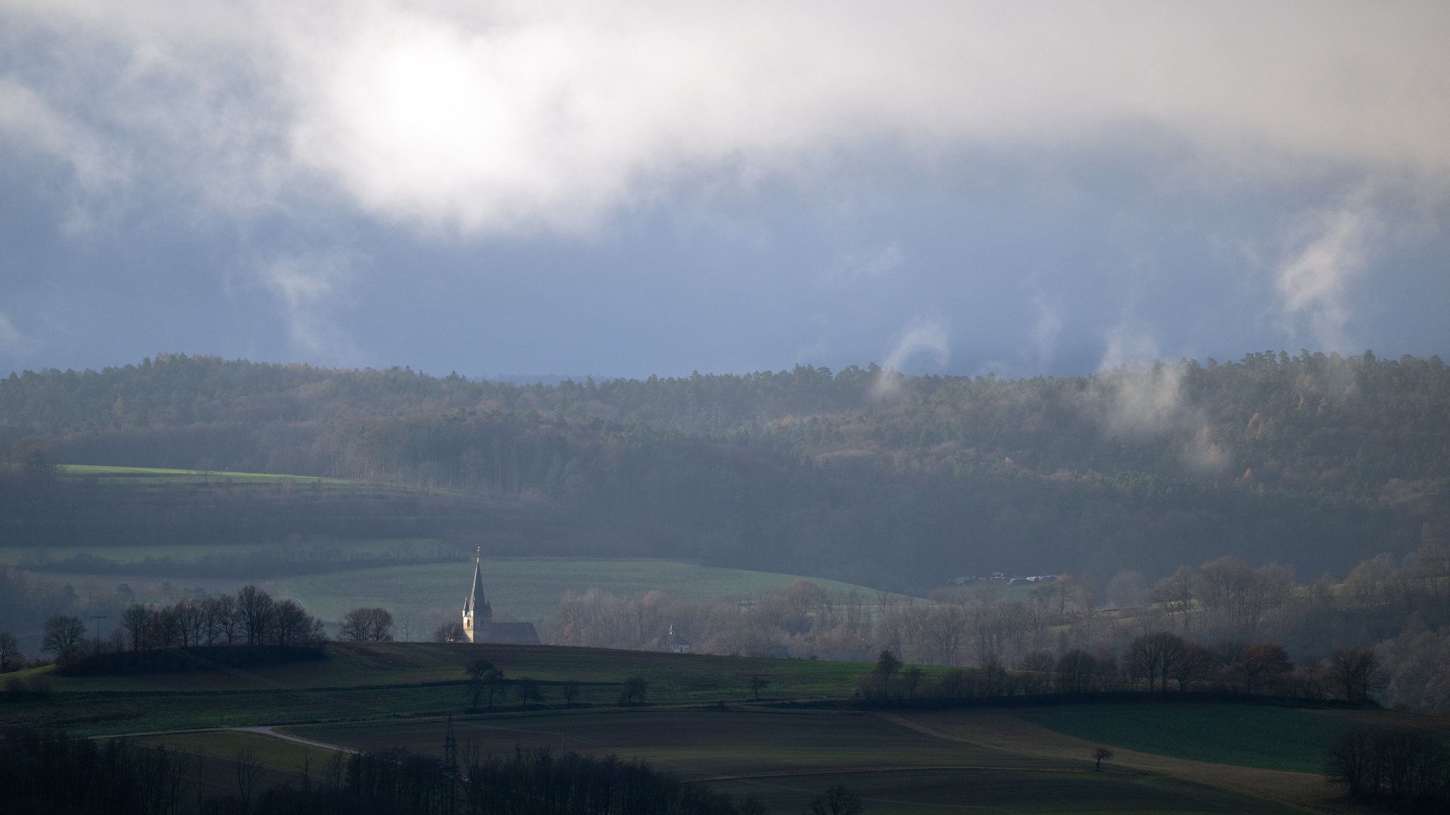 07.12.2025: Nebel steigt aus den Wäldern auf, während eine Kirche von der aufgehenden Sonne beschienen wird. | Bild: picture alliance/dpa | Pia Bayer 07.12.2025: Nebel steigt aus den Wäldern auf, während eine Kirche von der aufgehenden Sonne beschienen wird.
