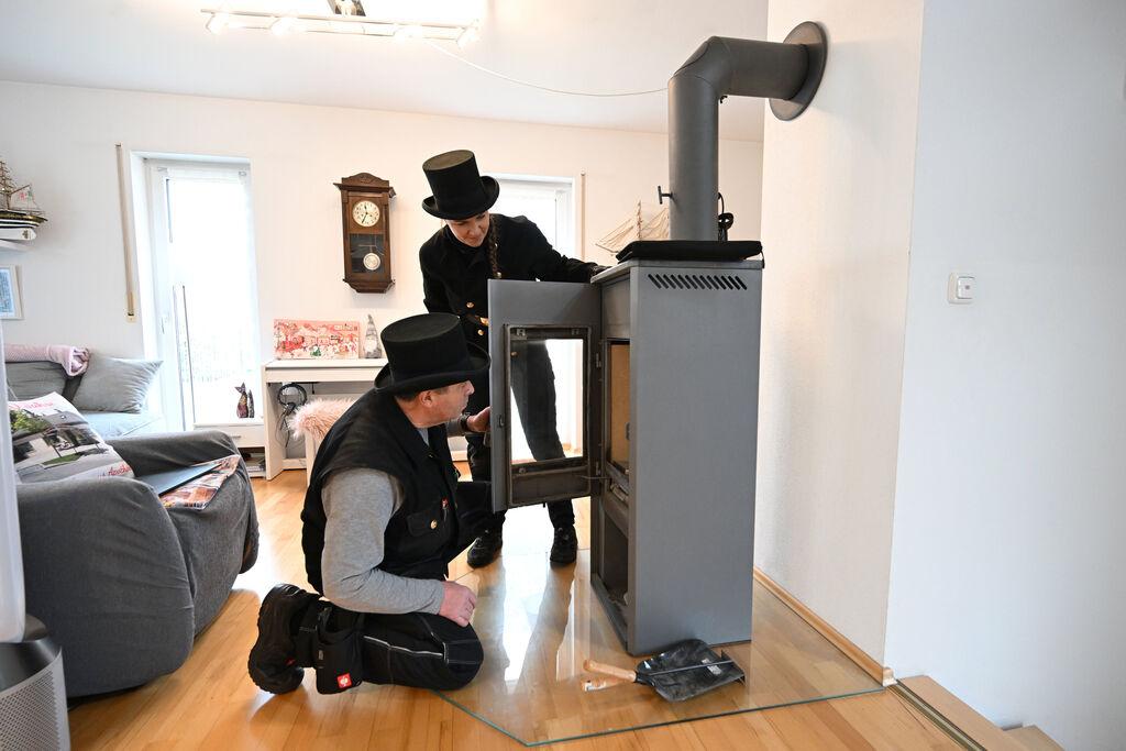 PRODUKTION - 13.12.2023, Bayern, München: Die Kaminkehrer Udo Löbel (l) und seine Tochter Diane Löbel begutachten einen Holzofen (Einzelraumfeuerstätte für feste Brennstoffe) in einem Einfamilienhaus. Ab Januar dürfen in Neubauten innerhalb von Neubaugebieten nur Heizungen eingebaut werden, die auf 65 Prozent erneuerbaren Energien basieren. Das dürfte in vielen Fällen eine Wärmepumpe sein. Foto: Felix Hörhager/dpa +++ dpa-Bildfunk +++