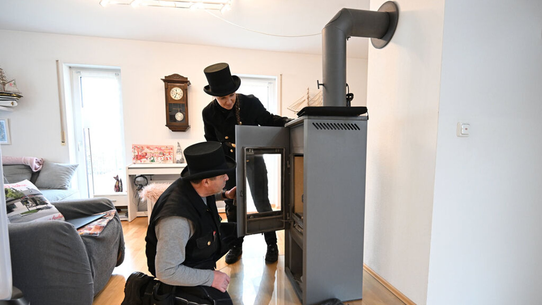 PRODUKTION - 13.12.2023, Bayern, München: Die Kaminkehrer Udo Löbel (l) und seine Tochter Diane Löbel begutachten einen Holzofen (Einzelraumfeuerstätte für feste Brennstoffe) in einem Einfamilienhaus. Ab Januar dürfen in Neubauten innerhalb von Neubaugebieten nur Heizungen eingebaut werden, die auf 65 Prozent erneuerbaren Energien basieren. Das dürfte in vielen Fällen eine Wärmepumpe sein. Foto: Felix Hörhager/dpa +++ dpa-Bildfunk +++