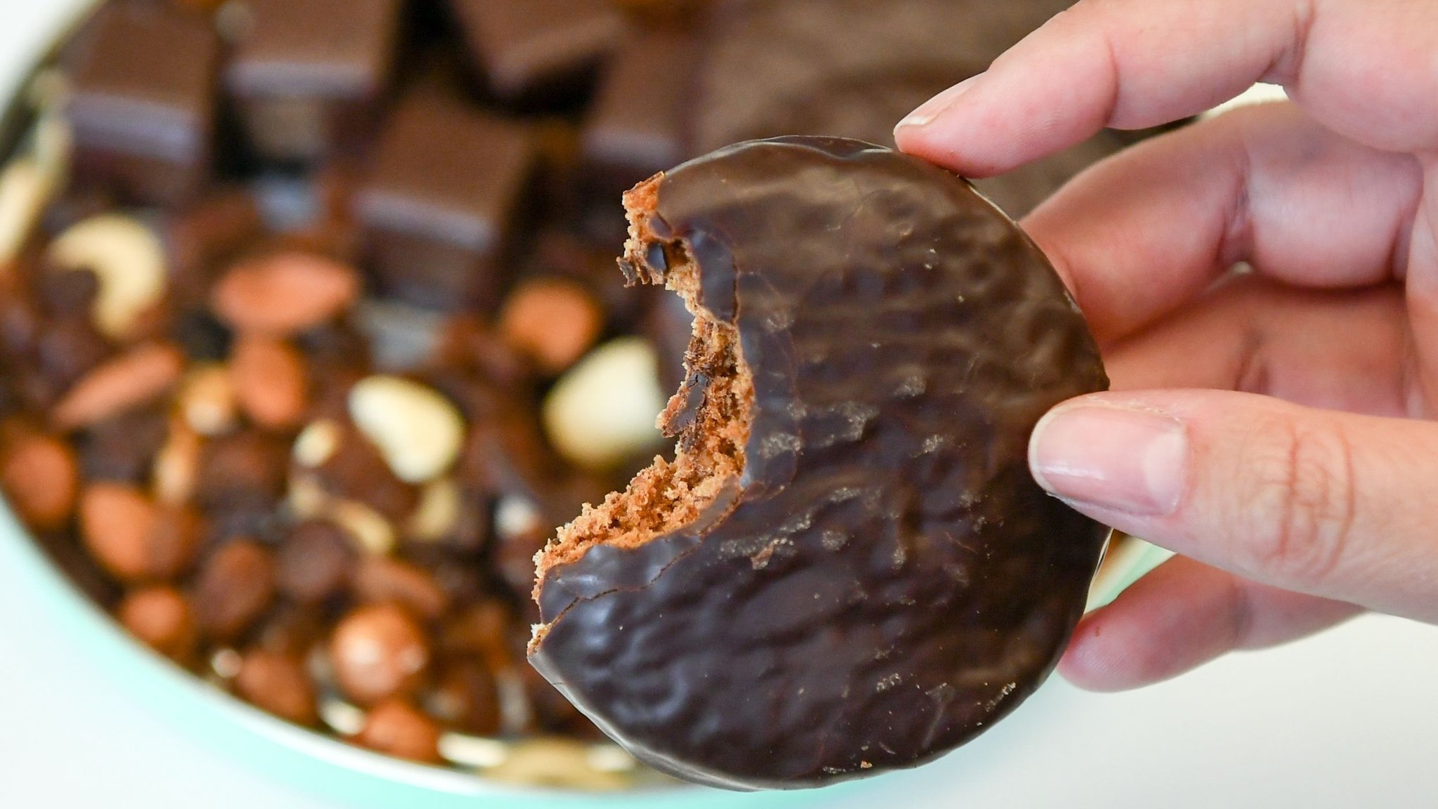 Frauenhand hält angebissenen Lebkuchen mit Schokolade in der Hand.