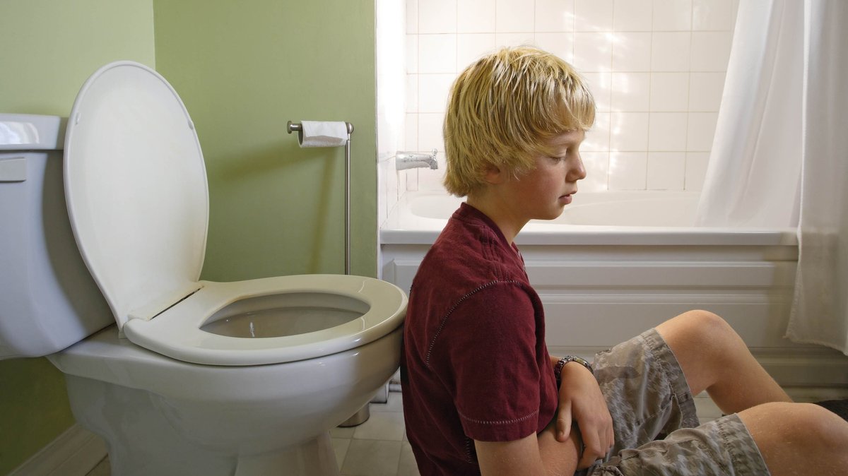 Junge sitzt mit dem Rücken auf dem Boden vor einer Toilettenschüssel