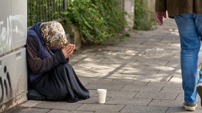 Ältere Dame beim Betteln am Straßenrand in München, betet für Unterstützung. Ein Passant läuft an ihr vorbei. Symbolbild Altersarmut | Bild: picture alliance / CHROMORANGE | Michael Bihlmayer Ältere Dame beim Betteln am Straßenrand in München, betet für Unterstützung. Ein Passant läuft an ihr vorbei. Symbolbild Altersarmut