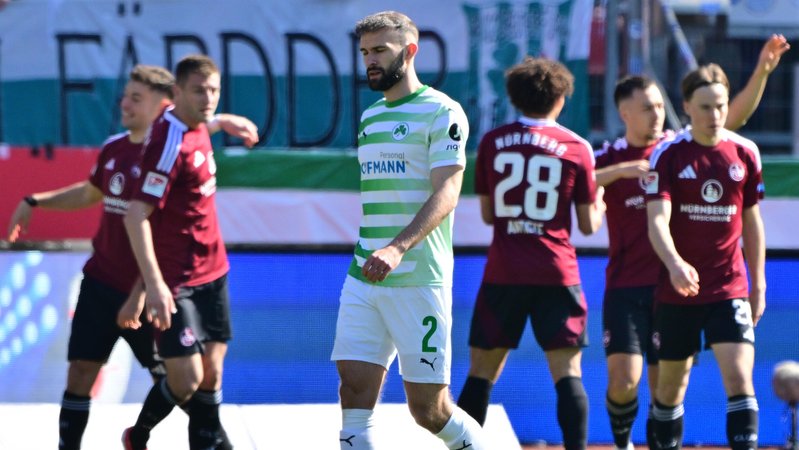 Fürths Simon Asta ist enttäuscht. Im Hintergrund jubeln die Nürnberger. | Bild: picture-alliance / dpa Fürths Simon Asta ist enttäuscht. Im Hintergrund jubeln die Nürnberger.