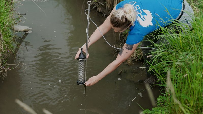 LBV-Studienleiterin Raphaela Karl platziert das Messgerät im Geislbach. Der Schwimmer kann bei Starkregen, wenn der Bach anschwillt, automatisch die Probe auslösen. | Bild: BR / Michael Barthelmess LBV-Studienleiterin Raphaela Karl platziert das Messgerät im Geislbach. Der Schwimmer kann bei Starkregen, wenn der Bach anschwillt, automatisch die Probe auslösen.