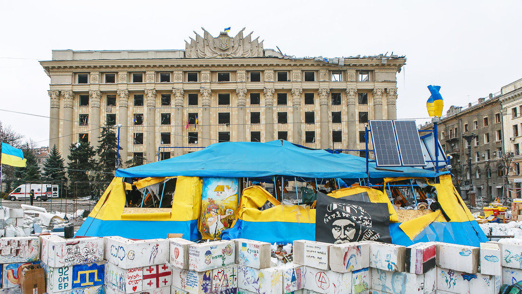 Ein zerbombtes Verwaltungsgebäude in Charkiw. Davor steht ein Zelt in den ukrainischen Farben blau und gelb
