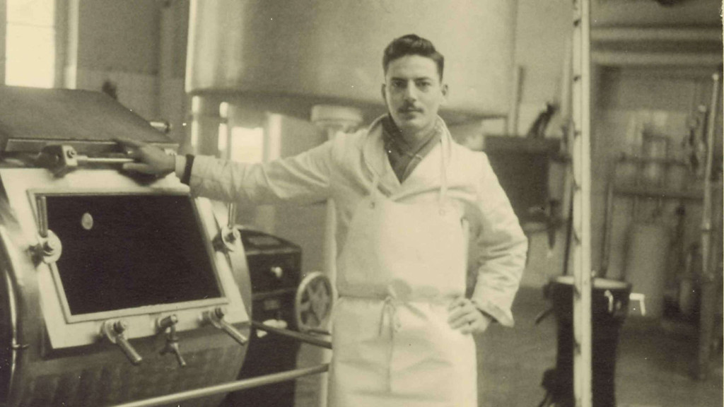 Schwarz-weiß Foto des jungen Michael Strauss vor einer Maschine in einer Fabrik des Unternehmnes.