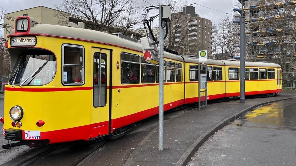 Alte, gelbe Straßenbahn mit einem dünnen roten Streifen in der Mitte und einem dicken roten Streifen unten.