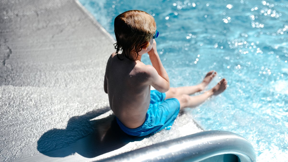 Ein Junge sitzt in einem Schwimmbad am Ende einer Rutsche (Symbolbild).